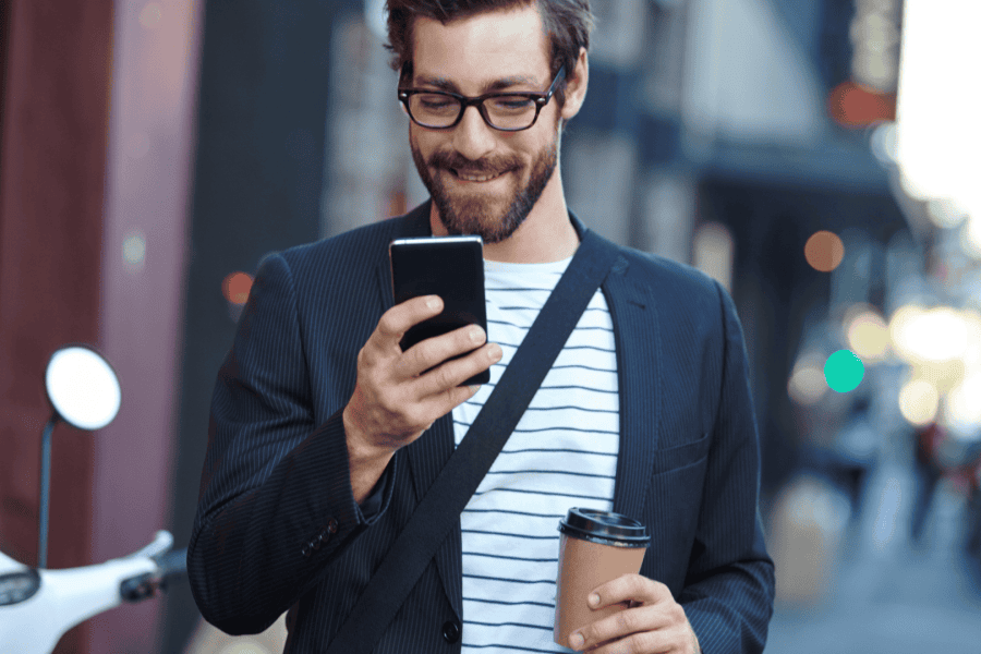 Eine Person auf dem Gehweg hält einen Kaffee in der Hand und lächelt, während sie eine Nachricht auf dem Handy liest – wenn E-Mail-Kampagnen gelingen.