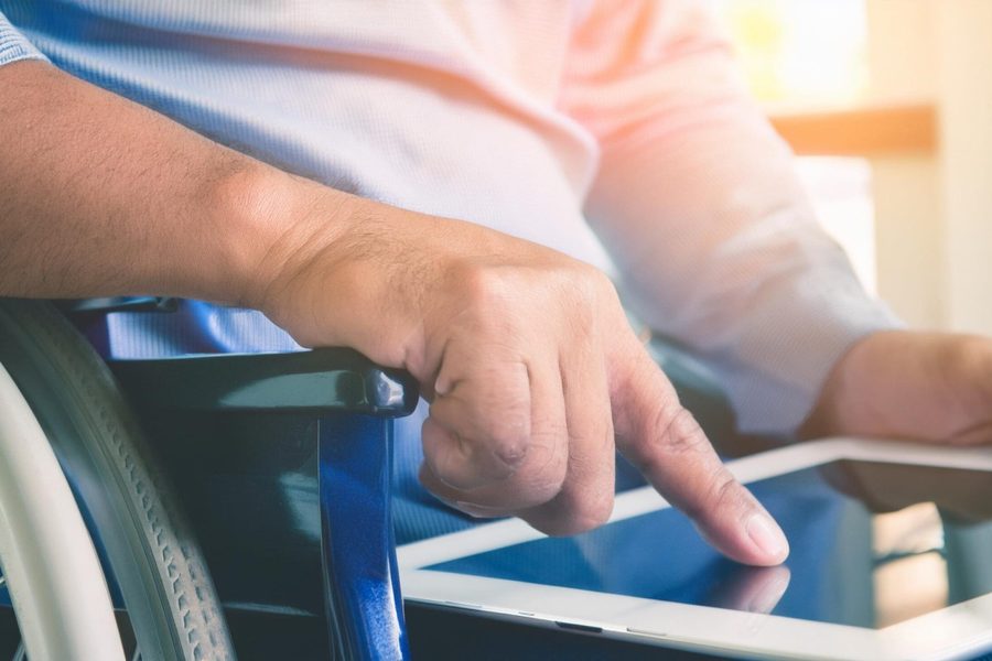 Barrierefreiheit im Online-Shop: Eine männliche Person im Rollstuhl streicht mit dem Finger über ein Tablet.